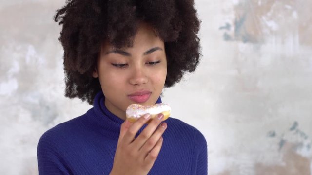 African young woman isolated on white eating donut licking fingers happy
