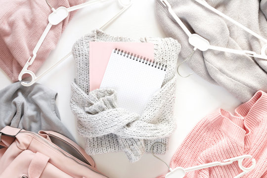 Winter creative flat lay.Knitted gray sweater with a notebook for writing and a set of pink sweaters on a white background with copy space, concept of winter shopping and discounts.