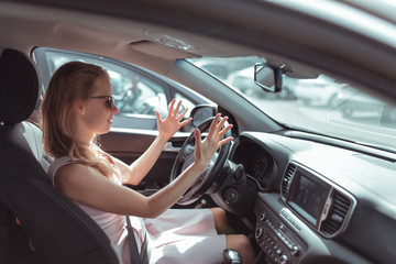 Girl driving car in cabin. Hand gesture accident signal conflict, emotions stress aggression discontent. Pink dress summer in parking lot mall. Misunderstanding scandal and accident on road.