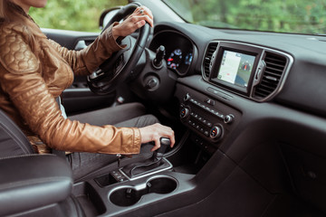 woman in summer autumn, driving car, parking reversing, engages automatic transmission. Start movement of car, inclusion of parking mode. Leather jacket, touch screen.interior of car.