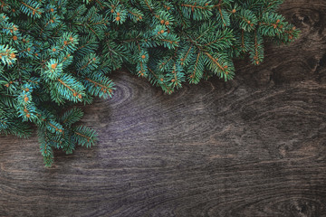Natural Christmas background with border of fluffy green fir branches on a textured dark brown wood background. Copy space for text, flat lay, top view. Corner frame.