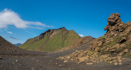 Panoramic volcanic desert landscape with lava rock formation and green Hattafell mountain with footpath of Laugavegur trail. Fjallabak Nature Reserve, Iceland. Summer blue sky