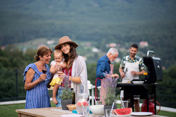 Multigeneration family with wine outdoors on garden barbecue, grilling.