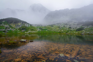 Wet stones on "Tăul Porții" lake coast in foggy  autumn morning. The fog spreads over the water.