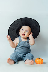 A small child in a black hat sits next to an orange little pumpkin. Halloween concept
