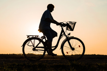 Fototapeta na wymiar Senior woman riding bike in nature, silhouette of riding woman at sunset