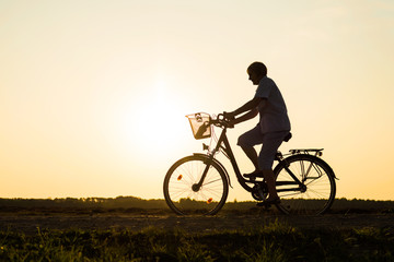 Obraz premium Senior woman riding bike in nature, silhouette of riding woman at sunset