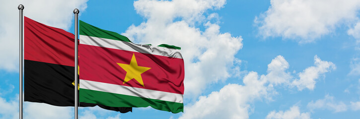 Angola and Suriname flag waving in the wind against white cloudy blue sky together. Diplomacy concept, international relations.