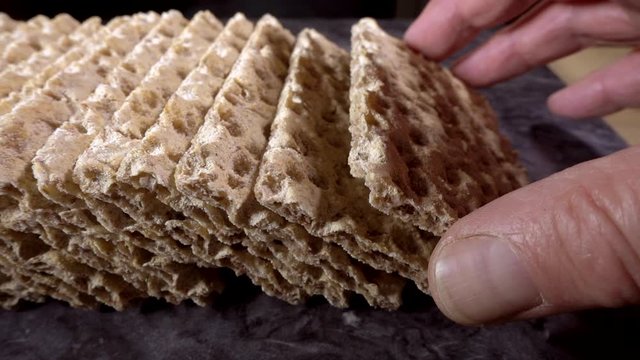 Normal speed then slow motion: Close POV dolly shot of a line of rye crispbreads, with fingers picking up the piece on the end.