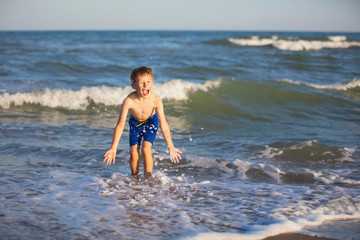 A child plays on the beach. A happy boy splashes the water of the sea. Active holiday on the beach