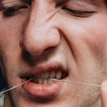 Close up view of young man pulling string between his teeth