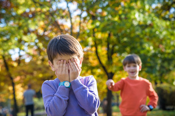 Pupil bullying another in the yard at the elementary school. Older boy offends younger kid. Laughing on his back. Small child closed face with hands and crying