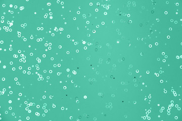 Shiny geometric foil confetti background. Shiny foil circles and stars sparse on trendy mint green colored paper. Simple holiday concept. Top view, flat lay