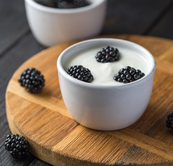 Fototapeta na wymiar Yogurt with blackberries on natural cutting board and wooden black table.