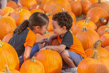 The small boy attempts to blend in down low with the pumpkins while his sister gets in his face to...