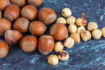 Top view of a group of whole and peeled hazelnuts on blue marble background in horizontal with copy space