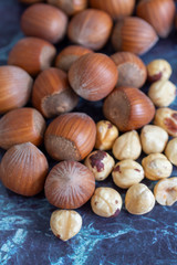 Top view of a group of hazelnuts, whole and peeled out of focus on focused blue marble background, in vertical