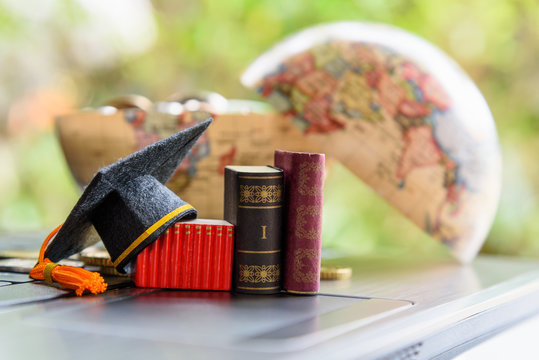 Graduate study abroad program for opening vision or expand world view concept : Graduation cap or hat, world globe map, foreign text book on laptop, depicts achievement or success in online education.
