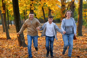 Happy family having holiday in autumn city park. Children and parents running, smiling, playing and having fun. Bright yellow trees and leaves