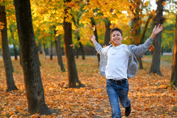 Boy teenager having holiday in autumn city park, running, smiling, playing and having fun. Bright yellow trees and leaves