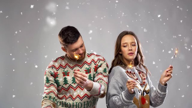 celebration, fun and holidays concept - happy couple wearing knitted sweaters with sparklers dancing at christmas party