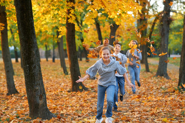 Happy family having holiday in autumn city park. Children and parents running, smiling, playing and having fun. Bright yellow trees and leaves