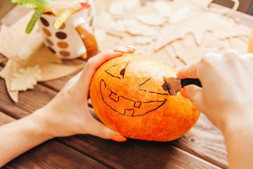 Woman’s hands carving with knife a pumpkin to Halloween decoration.