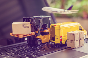Logistics, supply chain and delivery service concept : Fork-lift truck moves a pallet with box carton. Van on a laptop computer, depicts wide spread of products around globe in ecommerce popular era - obrazy, fototapety, plakaty