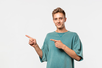 Handsome young man in a green tee showing with his fingers left at the empty space for advertising.