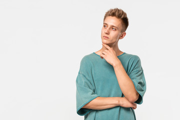 Thoughtful young man in a green tee looks up isolated over grey background.