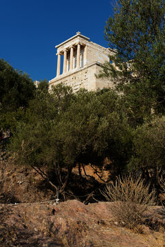 Temple of Niki Apteros in sunny weather. In the foreground is an olive grove. Ancient Greek temple on the Acropolis of Athens