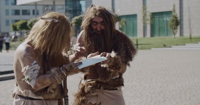 Shot of caveman in animal fur using modern tablet browsing internet having fun civilization computer device evolution future homo sapiens humanity hunter-gatherers neanderthals paleolithic slow motion