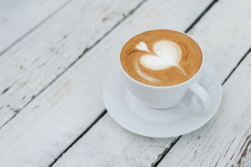 White big cup of coffee with shaped heart art on white wooden table with copy space.