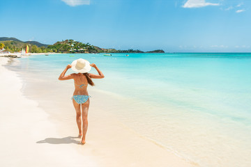Fototapeta na wymiar Beach travel vacation woman walking on luxury Caribbean cruise destination Antigua island in bikini wearing beach hat, carefree on holidays on Jolly Beach. Girl on travel vacation holidays swim model.