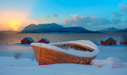 Beautiful winter landscape with snow covered green house at sunset - Red wooden boat covered with layers of snow - Tromso, Norway - Powered by Adobe