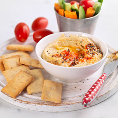 Hummus and fresh vegetables snack platter with crackers on a light background. Healthy snacks,...
