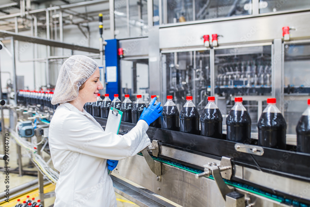 Wall mural young happy female worker in bottling factory checking juice bottles before shipment. inspection qua