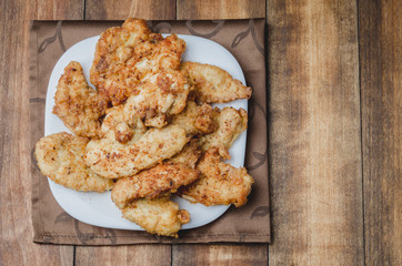 Fried crispy nuggets in a white bowl on a wooden table. Top view, copyspace. Chicken strips