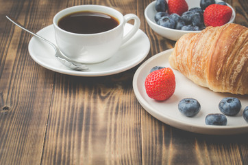 Delicious breakfast with cup of coffee and croissant with fresh berries. Wooden table.