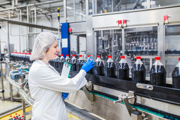 Young happy female worker in bottling factory checking juice bottles before shipment. Inspection quality control.