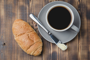 Coffee break with croissant butter knife and cup of black coffee on a dark wooden table. Top view.