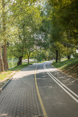 Bike path in the park with green trees. Beautiful summer landscape.