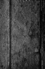 Close-up of a weathered and aged wooden door, wall or wood panelling in black and white with paint peeling off.