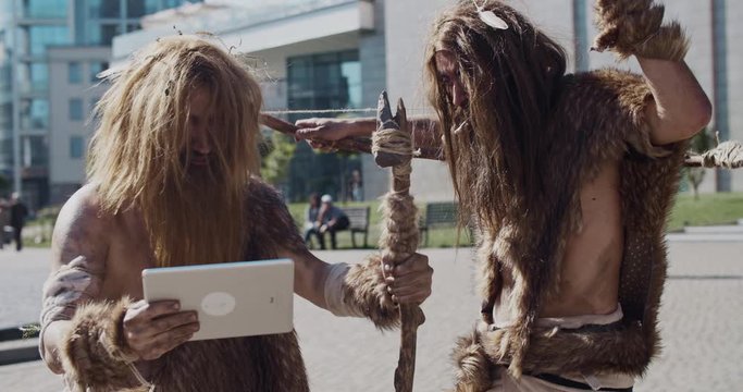 Angry caveman in animal fur using modern tablet browsing internet having fun civilization computer device evolution future homo sapiens humanity hunter-gatherers neanderthals paleolithic slow motion
