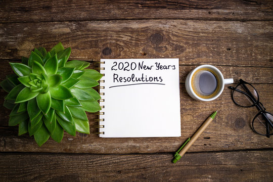 New Year Resolutions 2020 On Desk. 2020 Goals List With Notebook, Coffee Cup And Eyeglasses On Wooden Background. Goal, Plan, Strategy, Change, Idea Concept. Top View