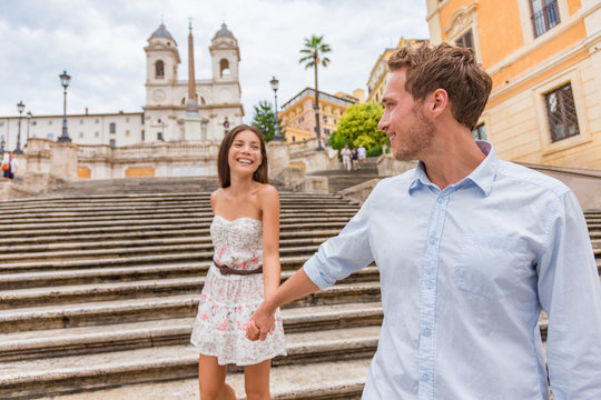 Happy Romantic Couple Holding Hands On Spanish Steps In Rome, Italy. Joyful Young Interracial Couple Walking On The Travel Landmark Tourist Attraction On Romance Europe Holiday Vacation.