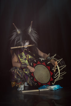 Taiko drummer in a wig and a demon mask on stage squarts with drumstick and drum on a black background. Demon from Japanese mythology.