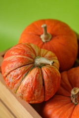 Orange pumpkins in a wooden box on a green background. Halloween, Thanksgiving, Harvest. Selective focus