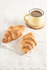 Crispy croissant and cup of coffee on a wooden table