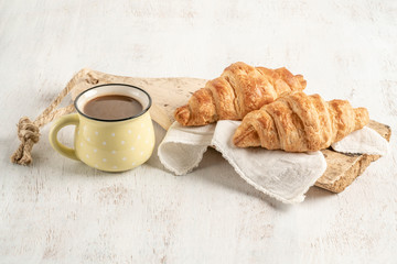 Crispy croissant and cup of coffee on a wooden table